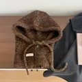 Detail van bruine gebreide bivakmuts met knopen en trekkoord op een houten oppervlak - Groen & Koffie