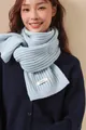 Dettaglio dell'etichetta 100% lana sulla sciarpa a maglia grossa in azzurro chiaro - Azzurro