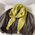 Lime green knitted scarf with pom poms on brown leather jacket for winter warmth - Yellow