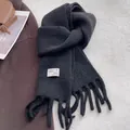 Detail of a black knit wool scarf featuring thick tassels and a woven brand label - Black