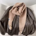 Detail of light camel ribbed knit scarf featuring soft pom-poms and brand textile label - Khaki