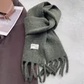 Close-up of dark green wool scarf with fringe and brand label on white furry background - Green