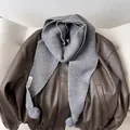 Detail of grey chunky knit hooded scarf featuring soft faux fur pom-poms on leather jacket - Gray