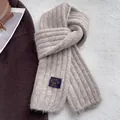 Macro detail of beige ribbed knit scarf texture with a woven brand label for winter warmth - Oatmeal Beige