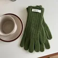 Close-up of moss green wool knit gloves with wavy edges and brand tag on a white desk - Green