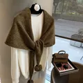 Detalle de una bufanda triangular de lana gruesa con pompones sobre un suéter blanco - Verde & Café