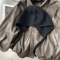 Détail d'une cagoule en laine bouclée noire avec protège-oreilles sur cuir marron - Noir