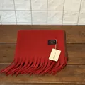 Detalle de bufanda roja de invierno con flecos, costura oscura y etiqueta de la marca - Rojo