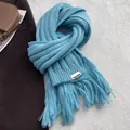 Thick light blue knit scarf with long tassels and minimalist patch on textured carpet - Lake Blue