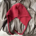 Detail of red textured wool balaclava hat with ear flaps and knit straps on leather jacket - Red