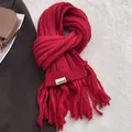 Detail of red chunky knit scarf with long tassels and woven label on textured fabric - Red