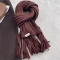 Detail of deep brown knit scarf showing thick fringe edges and designer fabric label - Coffee
