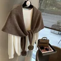 Detalle del chal de lana marrón grueso con pompones decorativos sobre un suéter blanco - Café Caqui