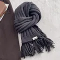 Close-up of charcoal grey knit scarf with long tassels and branding label detail - Black