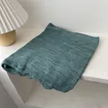 Detail of dark green crinkle texture shawl with raw edges on white wooden surface - Malachite green