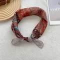 Detail of rust red paisley cotton linen scarf tied in a knot on a soft white texture - Khaki Edge