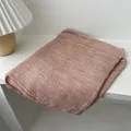 Detail of soft linen scarf in dusty pink folded neatly on a wooden desk with table lamp - 180x90cm / Pink
