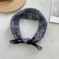 Close-up of a geometric black and white scarf tied in a knot on a beige textured background - Black