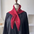 Detalle de bufanda triangular de lana roja con colgante metálico sobre un blazer negro - 100*30cm / Rojo