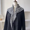 Chal de punto hueco gris en forma de triángulo sobre una chaqueta negra de doble botonadura - Gris