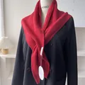 Detail of red chunky knit shawl wrap showing rich ribbed texture and brand tag on black blazer - Red