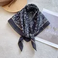 Detail shot of a black paisley square scarf with beige trim on a textured background - Black