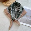Detailed macro view of dark green cashew floral paisley silk square scarf on a wooden tray - Dark Green with Pink Base / Green