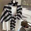Elegant black and grey striped wool knit shawl draped over a white blouse on a hanger - Striped