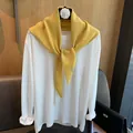 Detail eines gelben Wollstrickschals mit Metallemblem auf weißem Langarmshirt - Gelb