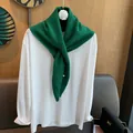 Detail view of emerald green 100% wool knitted scarf with silver button on white shirt - Green