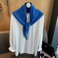 Detail eines blauen Wollstrickschals über einem weißen Langarmshirt auf einem Bügel - Blau