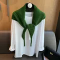 Détail d'une écharpe triangle en laine verte ajourée avec texture en maille et étiquette - Vert