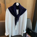 Detail eines dunkelblauen Woll-Dreieckstuchs, drapiert über ein weißes Langarmshirt - Marineblau