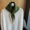 Close-up of dark green knitted triangular scarf with cream edges and silver buckle detail - Green