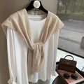Detailed knit texture of a beige wool shawl with ribbed edges on a white long sleeve top - Oatmeal