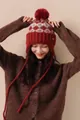 Close-up of red Fair Isle knit beanie with pom-pom and metallic emblem detail - Red