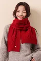Detail of red cable-knit merino wool scarf featuring golden fiber accents and metal logo - Berry Red