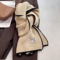 Detail of wool knit scarf with black contrast edging and white brand label on beige fabric - Off White