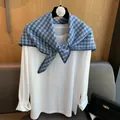 Detail of blue plaid woven triangle scarf with navy hand-stitched edges over a white tee - Blue