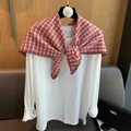 Detail of red and white checkered knitted triangle scarf styled on white long sleeve top - Red
