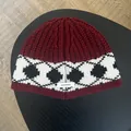 Close-up of 100% wool label on thick burgundy and black diamond knit beanie hat - Red