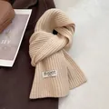 Detail of cream knit wool scarf featuring ribbed texture and stitched brand label - Apricot