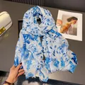 Dettaglio di sciarpa blu e bianca con motivi a foglia, texture dorate e bordi a frange - Blu