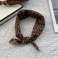 Detail of brown leopard print silk scarf tied in a knot on a quilted white backdrop - 70x70cm / Leopard Coffee