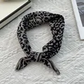 Close-up of leopard print silk scarf tied in a decorative knot on a textured white surface - 70x70cm / Black Coffee Leopard