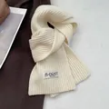 Close-up of cream white wool scarf showing ribbed knit texture and woven brand label - Cream White
