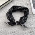 Detail of a black paisley silk scarf with a white border and knotted decorative styling - 70x70cm / Paisley Black