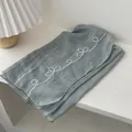 Close-up of grey-green linen scarf with white floral embroidery on a white desk - Light Blue