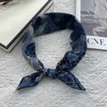 Detail of navy blue floral silk scarf tied as a headband on a white lace background - Aqua