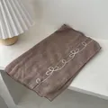 Detailed close-up of brown linen scarf with white embroidery in a cozy home setting - Coffee